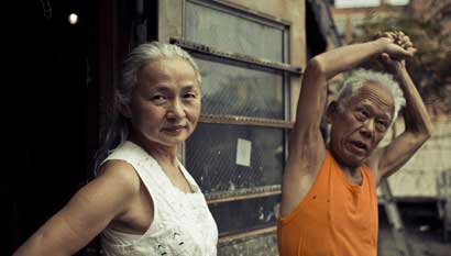 CUTIE_Noriko_Ushio_Shinohara_stretches Noriko Shinohara (l.) looks in the camera as her husband Ushio stretches. From Zachary Heinzerling’s CUTIE AND THE BOXER, a documentary about the 40-year marriage of artists Ushio and Noriko Shinohara. Photo credit: Erik Jonsso