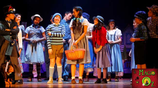 Una scena del musical Il Mago di Oz: il Sindaco e gli abitanti danno il benvenuto a Dorothy nel Paese dei Mastichini Una scena del musical Il Mago di Oz: il Sindaco e gli abitanti danno il benvenuto a Dorothy nel Paese dei Mastichini